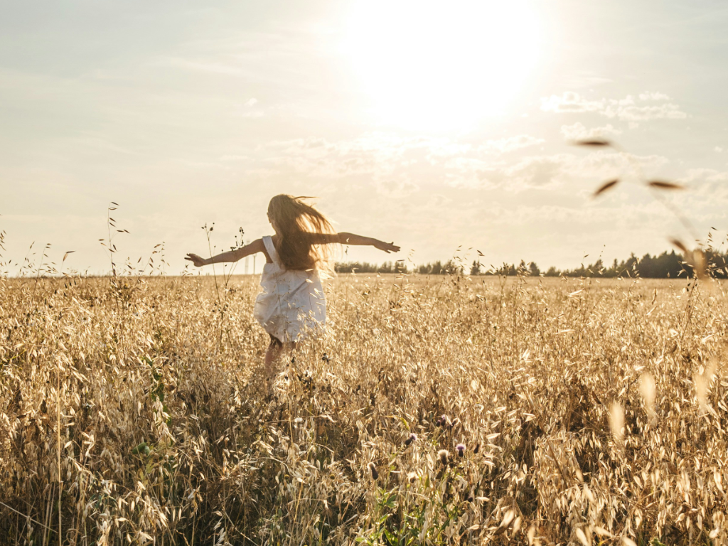 junge Frau springt befreit im Kornfeld, das sich im goldenen Sonnenlicht wiegt.